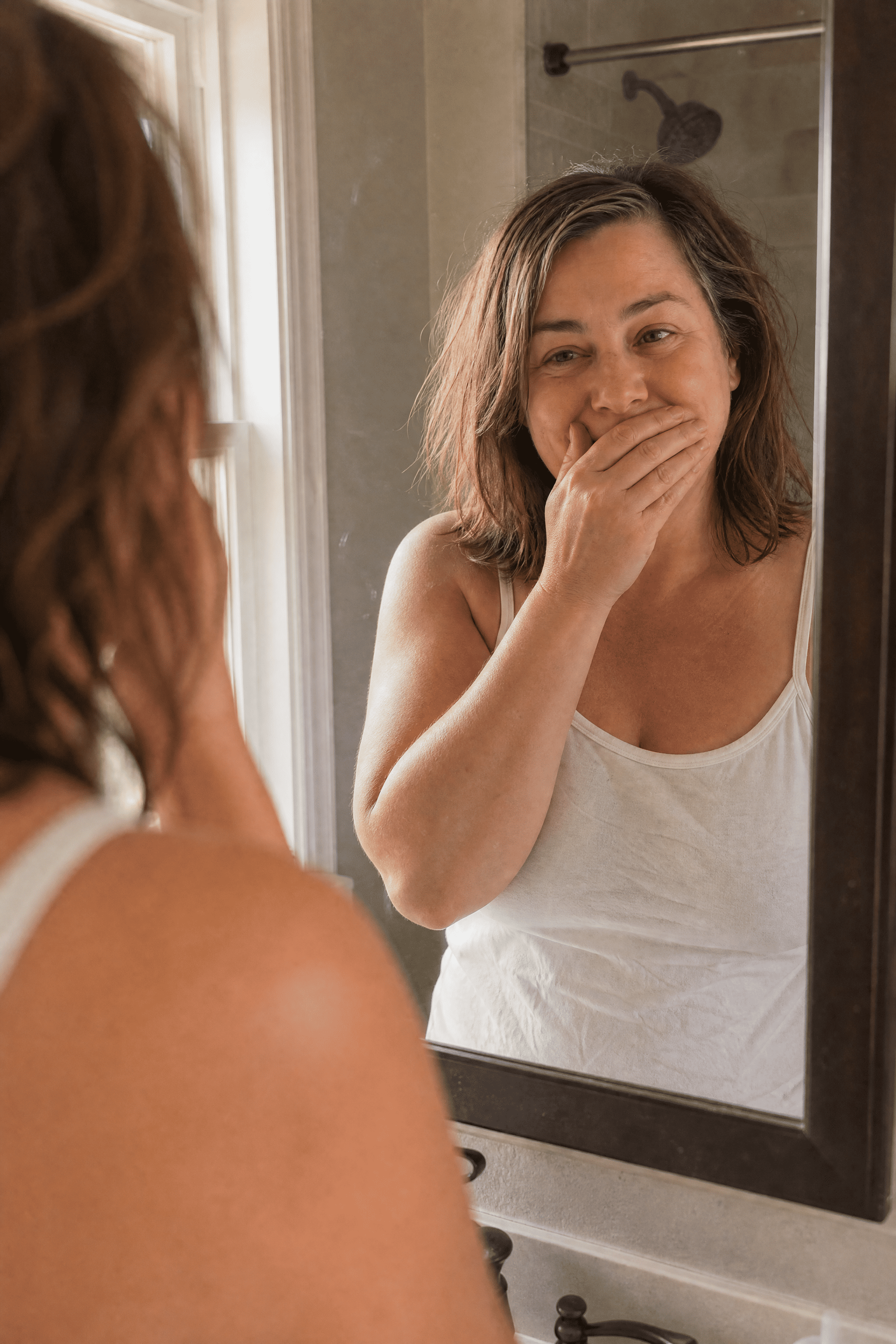 Tania at the bathroom mirror, hand over her mouth, stunned by her less-puffy, more-defined face